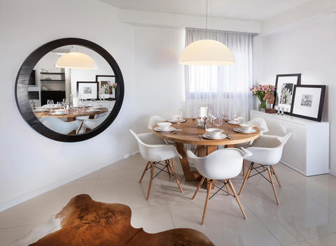 Apartment for Reuveni home styling & design. Modern dining room with wood table and white chairs. Table reflected in mirror hanging on wall.