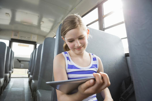 Smiling girl looking at digital tablet inside school bus