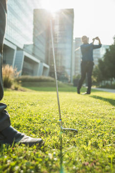 Two businessmen playing golf outside office building