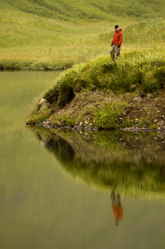 Athletic male hiker admires tranquil lake on Unalaska Island, Alaska.