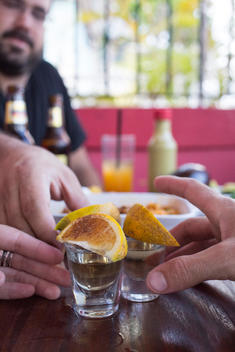 people reaching for shot glasses with tequila with orange wedges sprinkled with cinnamon