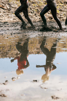 Low section of women running through muddy puddle