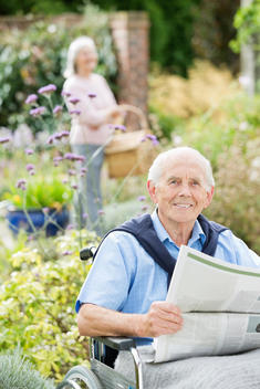 Older man in wheelchair reading newspaper outdoors