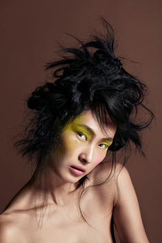 Asian model with lime green Eyeshadow pigments thrown all over her eyes, while wearing her hair upward.