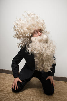 Man in blue suit with Santa Clause hair and beard is kneeling down and headbanging.