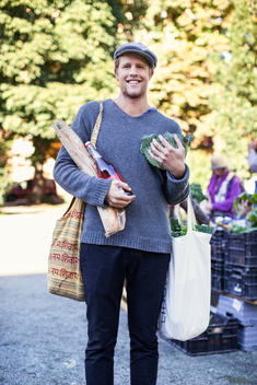 Portrait of smiling man holding groceries in market