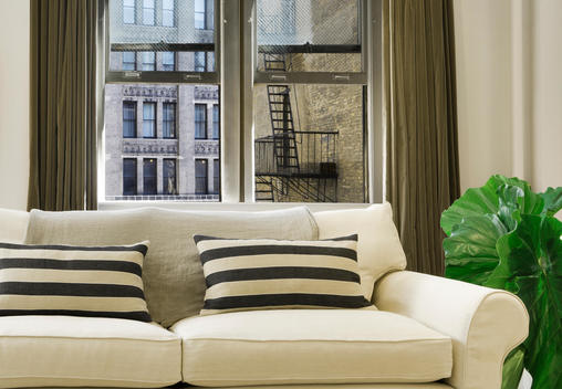 White Couch With Pillows And View Out Safety Glass Facing Fire Escape And Old Building