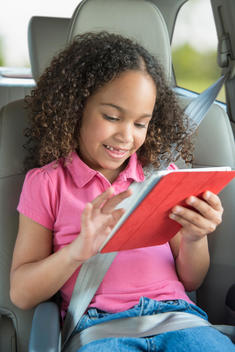 Mixed race girl using digital tablet in backseat of car