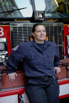 A Woman Firefighter Leans Against A Fire Engine.