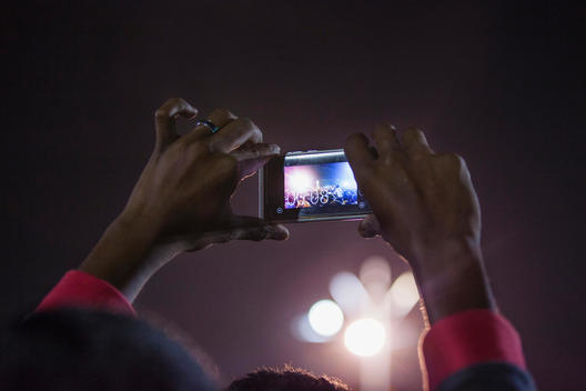 Mans hands holding camera phone to photograph crowds of people on New Years eve in Kochi, Kerala, India