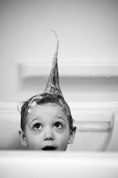 Girl (3-4 years) taking a bath and looking up at spiked hair.