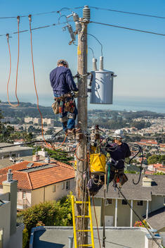 Electricians hanging on a power poll fixing power lines and a transformer.