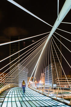 A young lady crossing Campo Volatin bridge at night designed by Santiago Calatrava, Bilbao, Spain.