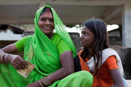 portrait of an Indian woman wearing sari nose ring and bindi and holding rupees in her hand and her daughter smiling at her