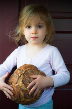 Toddler girl holds freshly baked, home made loaf of bread.