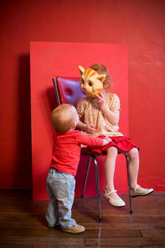 Girl and baby brother playing with cat mask.