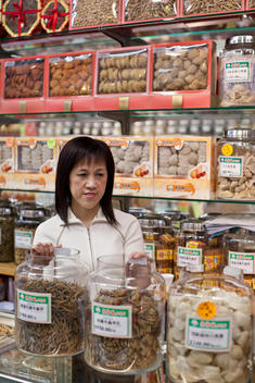 A Cashier Stands Behind Counter At A Chinese Herb Shop.