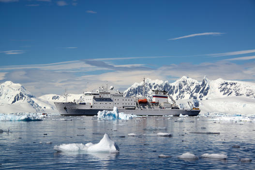 An Antarctic cruise ship with inflatable zodiacs on the calm waters among ice floes and mountainous landscape.
