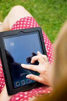 Young woman sitting in a garden chair touching display of digital tablet, partial view