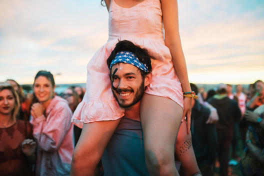 young man carries girl on shoulders in a crowd