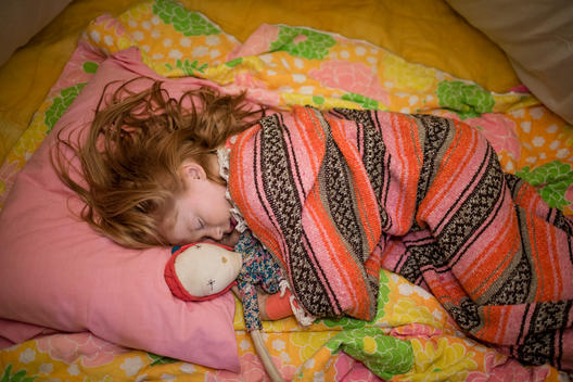 girl and doll sleeping under blankets