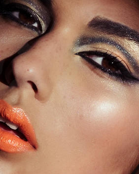 Close up beauty shot of a Indian woman with brown eyes. She has orange lipstick on and black eye liner around her eyes with gold eye shadow