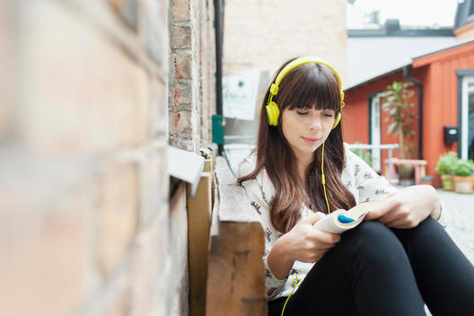 Young woman listening music while reading book at cafe backyard