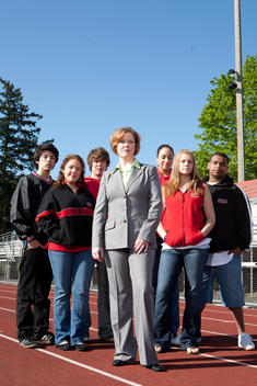 A Group Of Teenage Students And A Female Teacher Standing On A Track Looking At The Camera