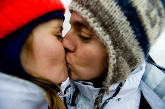Couple wearing knitted hats and kissing.