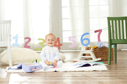 toddler in front of cut out numbers 1 to 7 in a living room playing and smiling