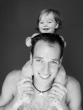 Smiling nine month old baby boy sitting on fathers shoulders and pulling his hair.