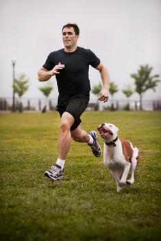Caucasian man in 20\'s or 30\'s running with dog in park