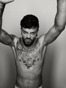 Portrait of angry man with tatoo on his chest stretching out his arms