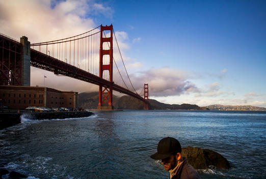A man wearing a black hat walking near the Golden Gate Bridge