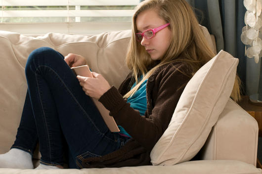 Pre adolescent girl reading book on sofa
