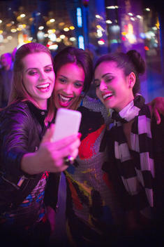 Women talking picture together using cell phone at night
