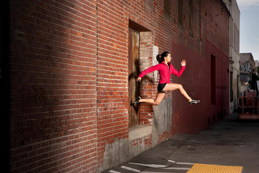 Woman jumping out of window, into alley, in a running pose
