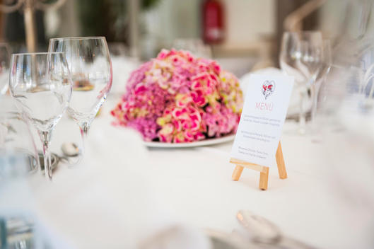 Table with wine glasses, menu and flower arrangement at wedding reception