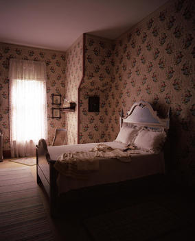 Interior Of An Old Fashioned Bedroom With Pink Wallpaper & Clothing Laid Out On The Bed