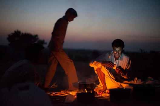 An Indian man checks his mobile phone whilst sat by a fire in the Thar Desert, Rajasthan, India.