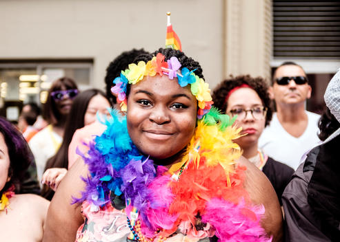 A woman with a rainbow feather boa and headband watches the 2015 NYC Pride March (Gay Pride Parade).