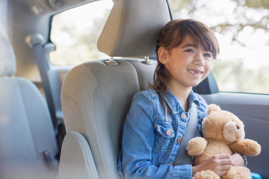 Happy girl with teddy bear in back seat of car