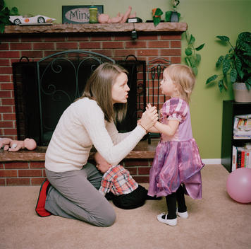 A young mother crouches down to reprimand her daughter, who wears a purple princess dress, for misbehaving and breaking the rules