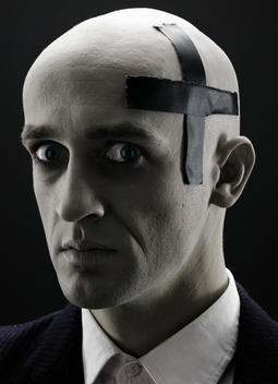 Bald man with cross made of electrical tape on his head expresses fear
