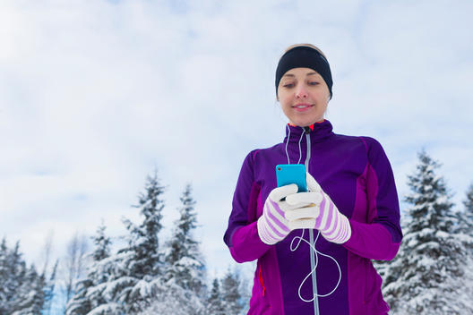 Adult female runner selecting her play list on her smart phone while getting ready for her run on snow covered road.