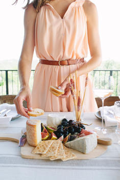 Woman in pink dress putting together cheese plate.
