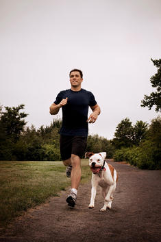 Caucasian man in 20's or 30's running with dog in park