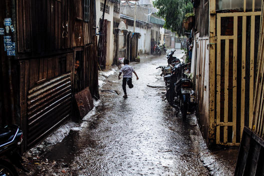 A child runs down an alley during a rainstorm in an impoverished neighborhood of Phnom Penh, Cambodia, near Empowering Youth in Cambodia\'s Lakeside School.