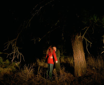 Couple Embrace In Woods At Night, Illuminated By Headlights
