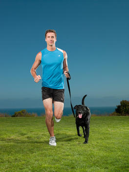 A male jogger runs with his black Labrador on a leash
